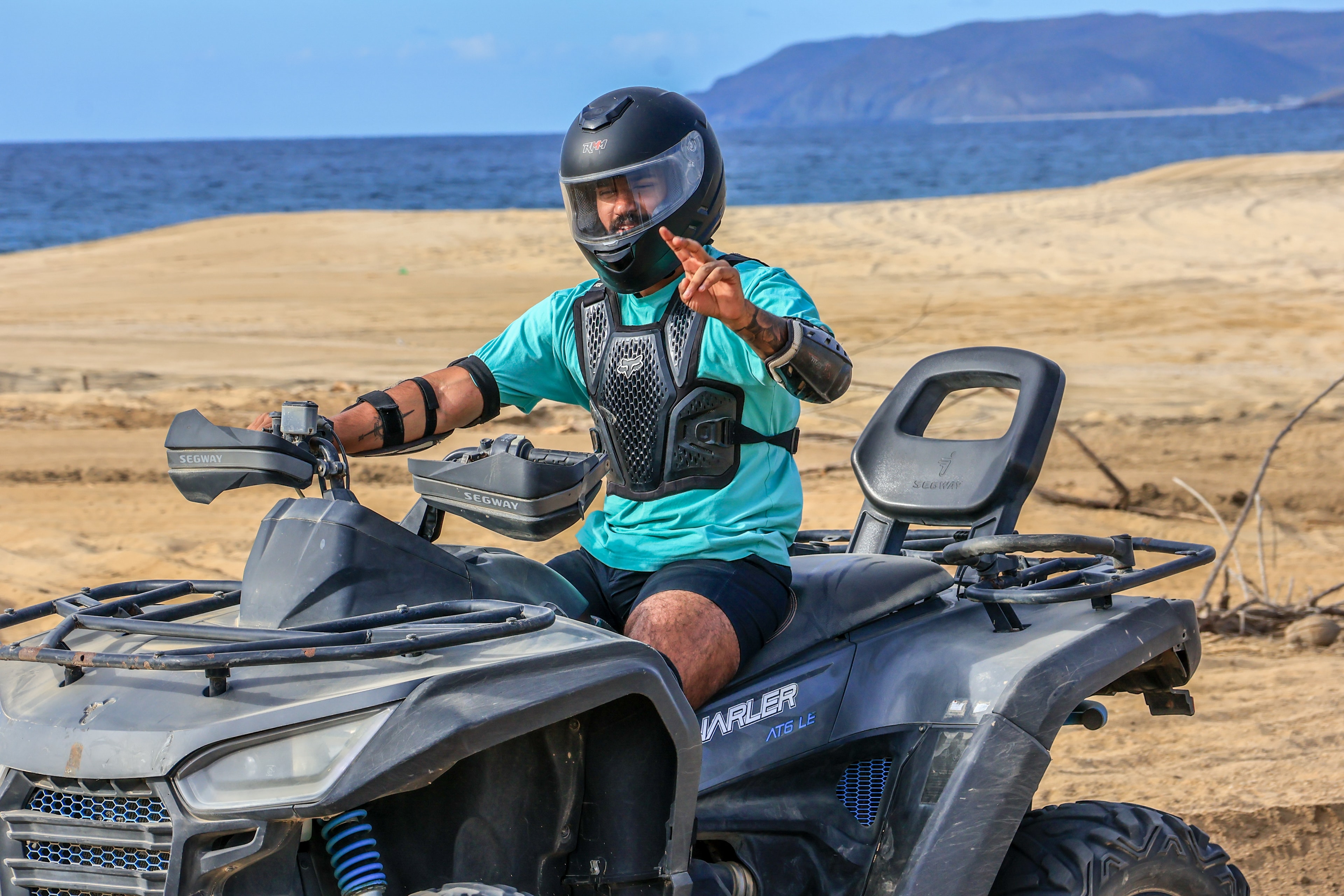 Pranav Saravanan riding an ATV on a beach with mountains behind him